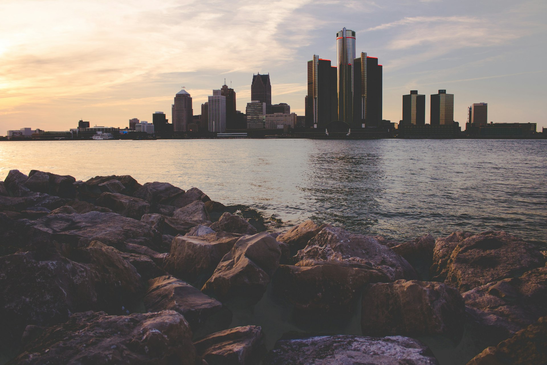 The Detroit riverfront at golden hour with a rocky shoreline in the foreground