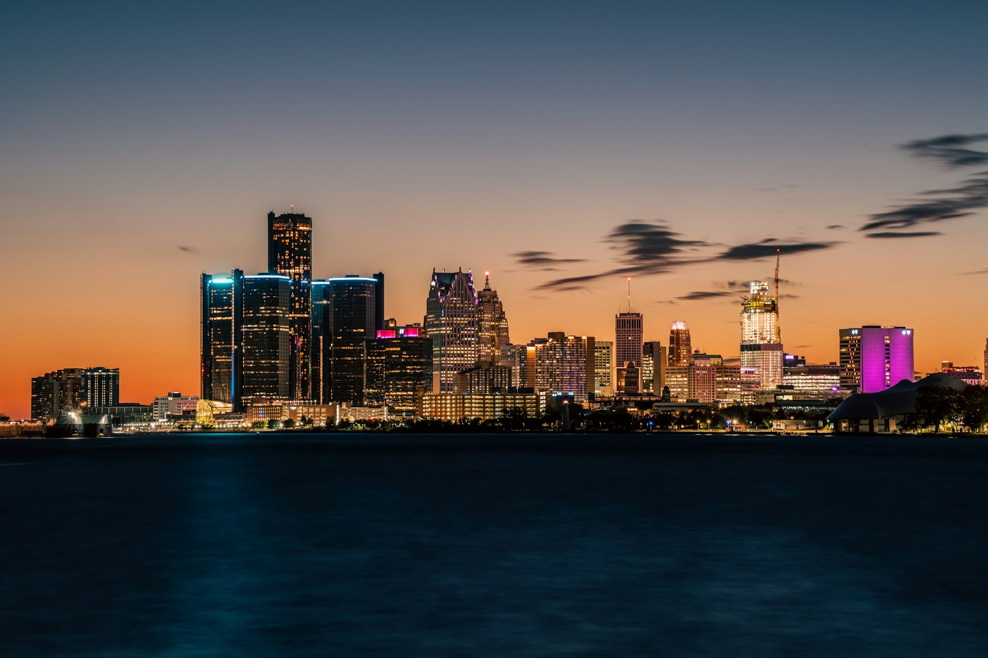 The Detroit skyline at dusk, illuminated towers reflected over the Detroit River